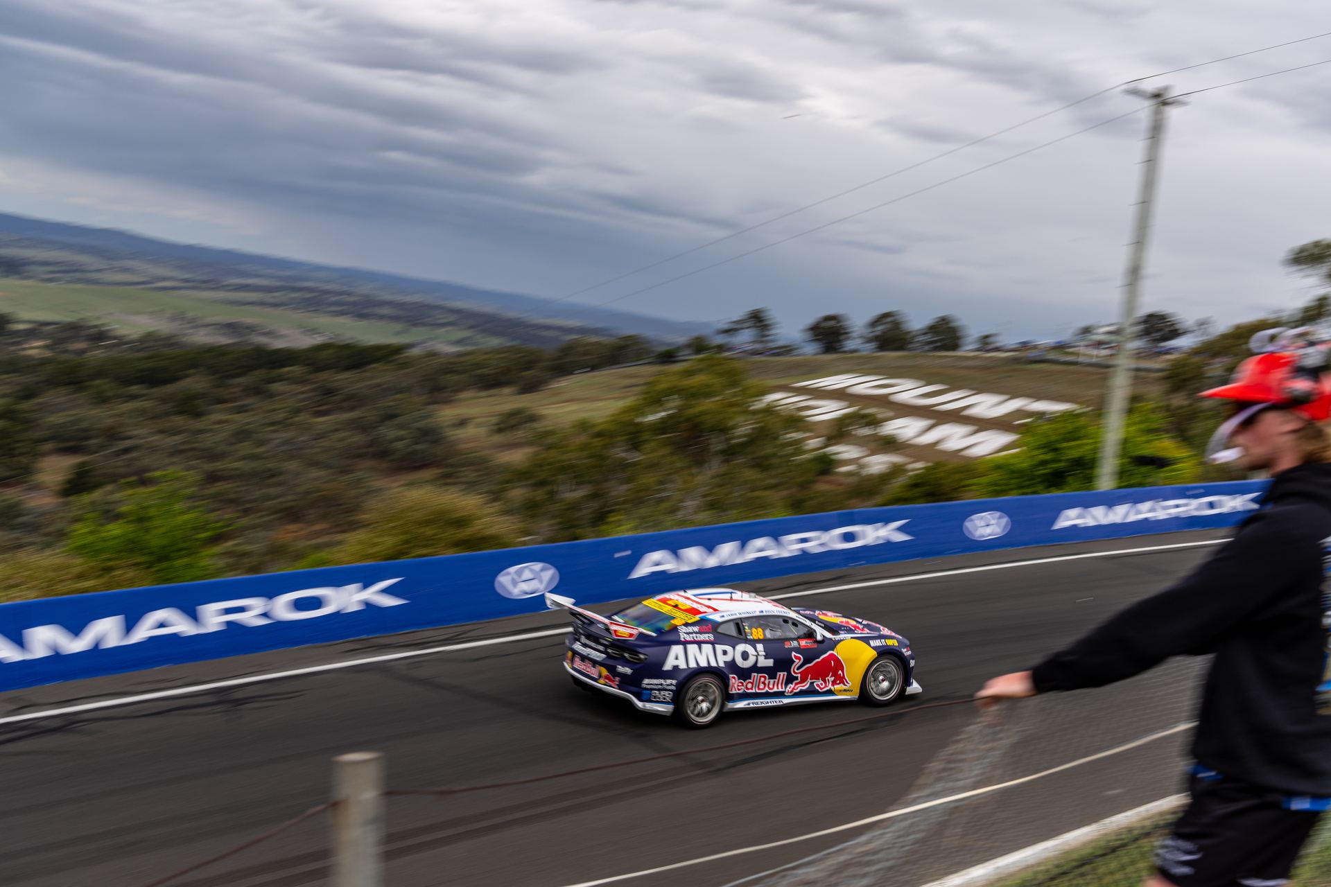 A fan at the fence watches a Supercar climb the mountain at Bathurst